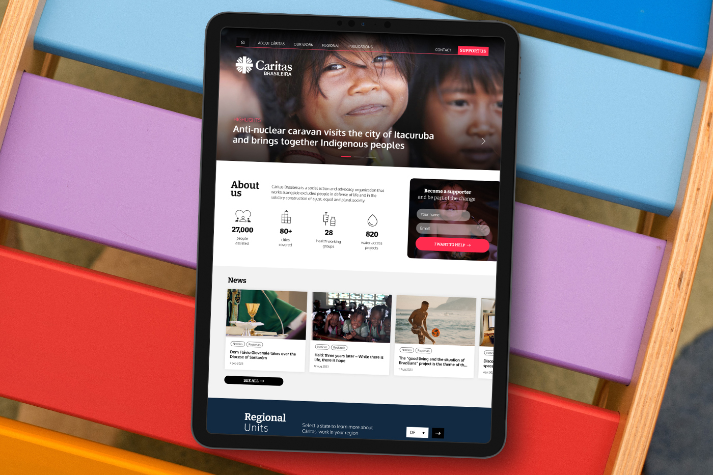 The Caritas Brasileira homepage on a tablet resting on colourful chairs