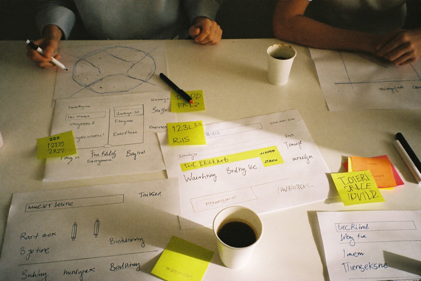 Paper wireframe sketches, sticky notes, and markers on the sprint table
