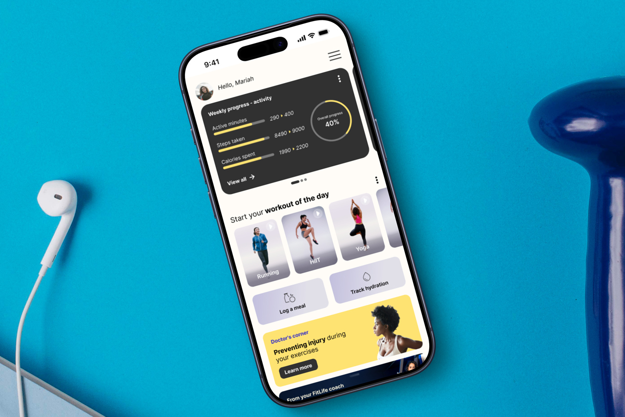 FitLife home screen on an iPhone, lying on a blue surface next to earphones and a dumbbell